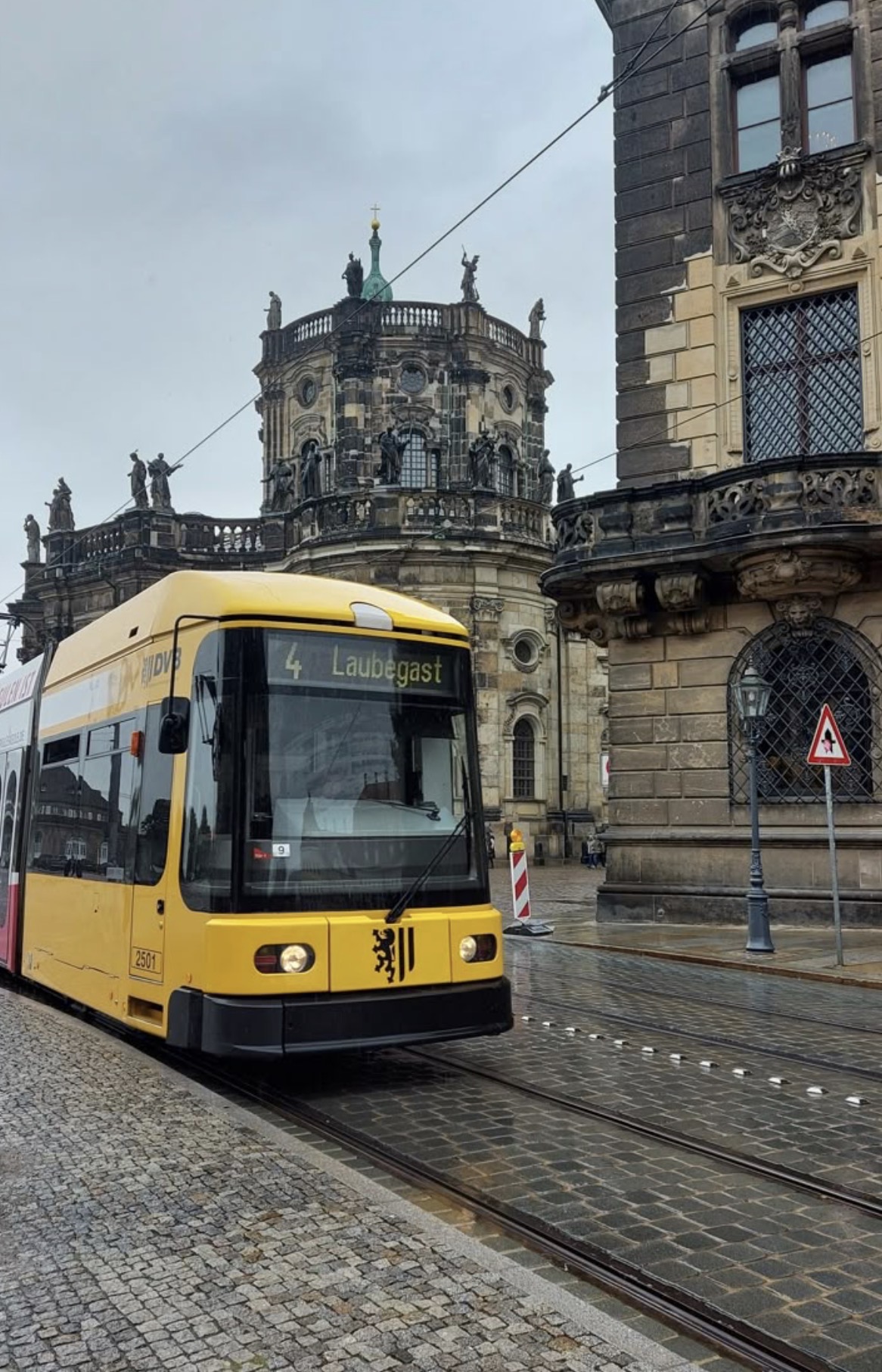 A yellow tram on wet cobblestone tracks past old stone buildings